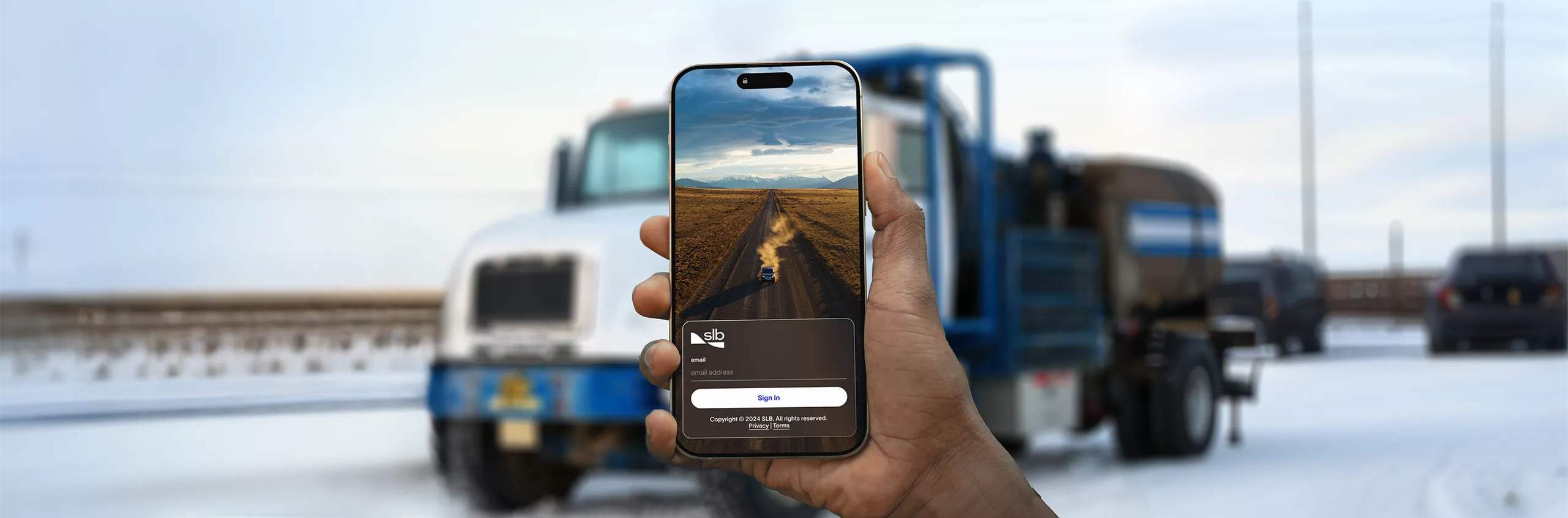 A field worker signing in to the SLB Customer app on a phone, in front of a service truck on site.