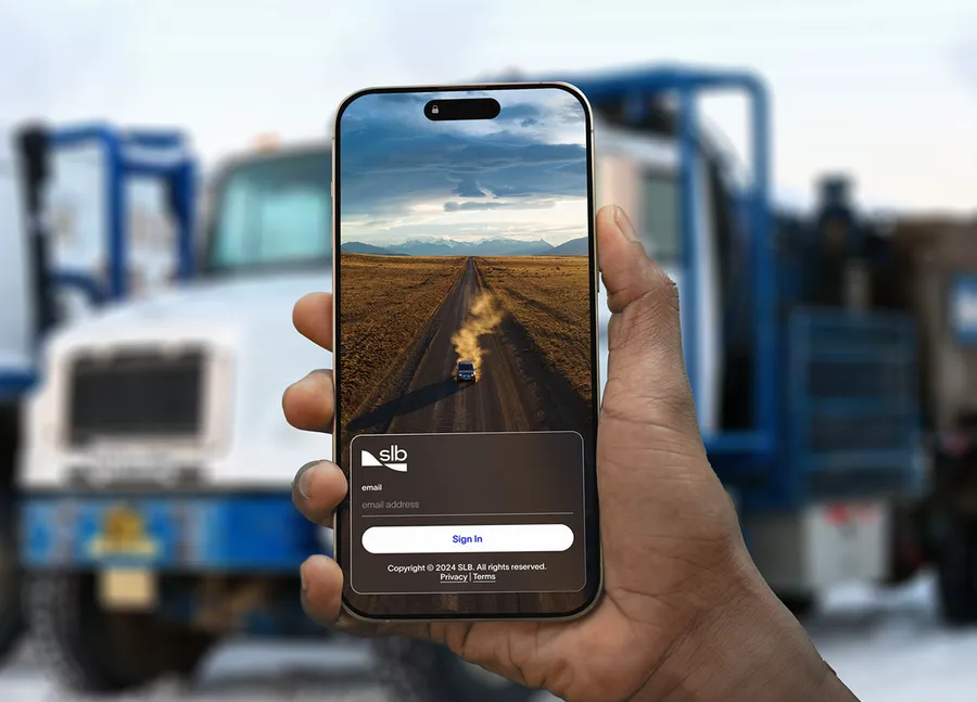 A field worker signing in to the SLB Customer app on a phone, in front of a service truck on site.