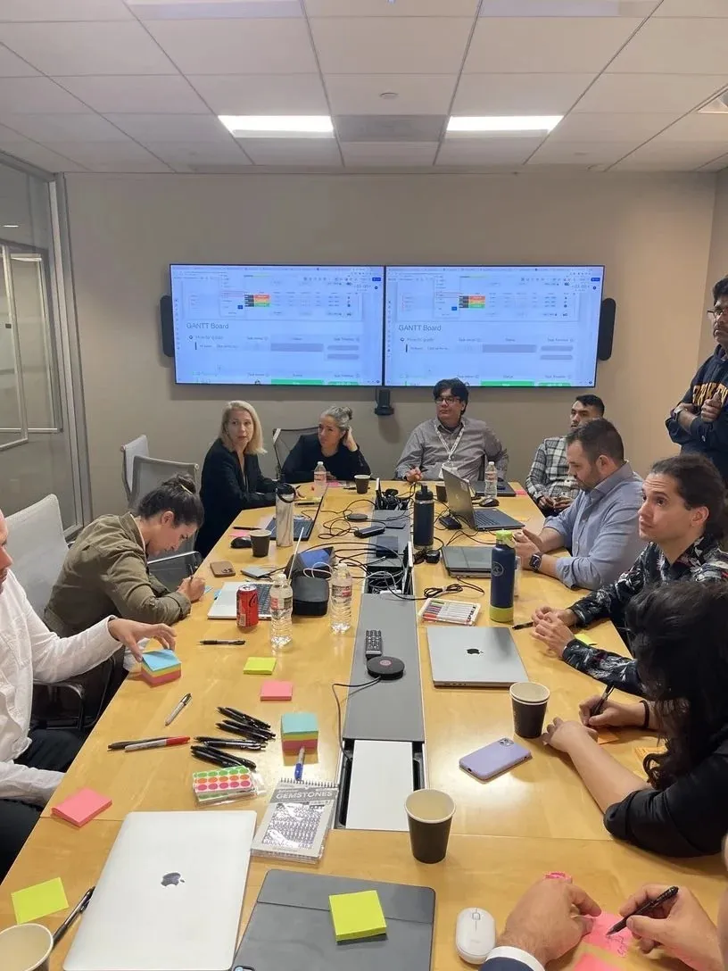 The team around a table with sticky notes and markers, a Gantt board on the screens behind them.